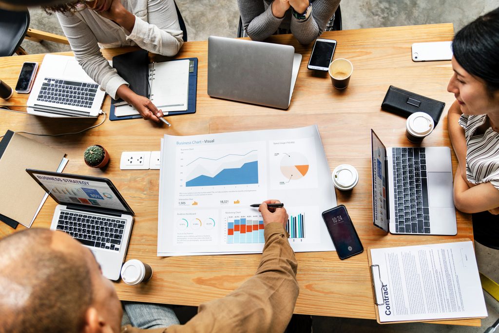 Mesa de reunião com pessoas expondo gráficos positivos da empresa